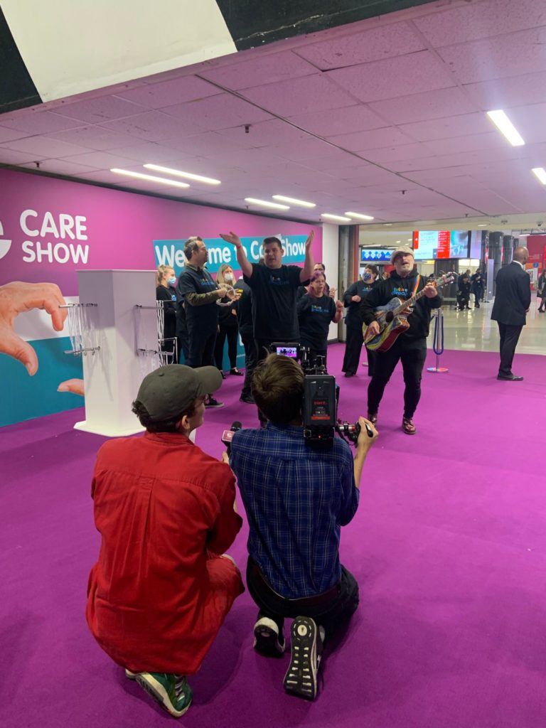 Stronger together choir on the purple carpet with camera men recording them